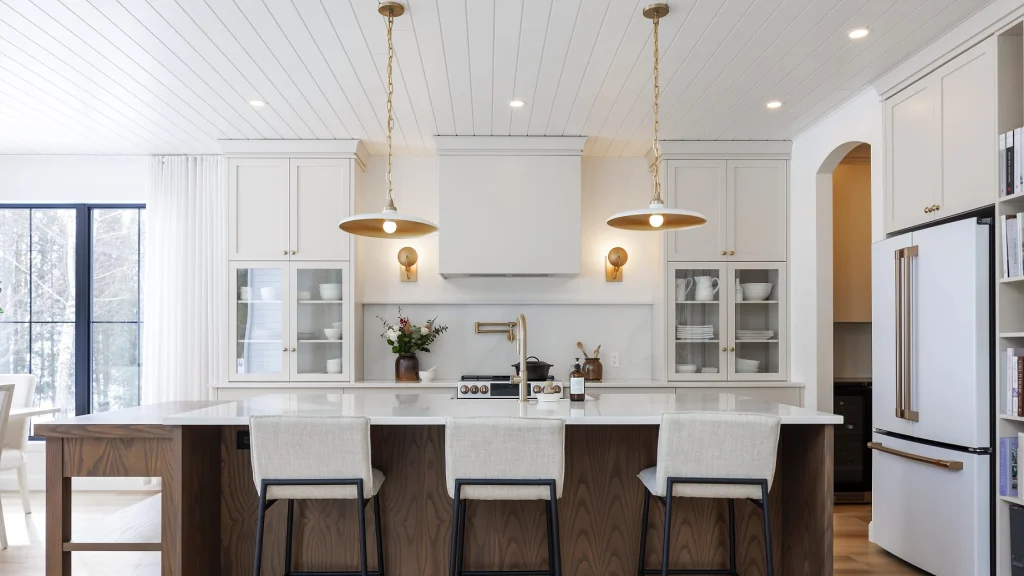 Cream-white custom kitchen cabinets with glass doors, paired with a white-topped wood island and brass pendant lights.