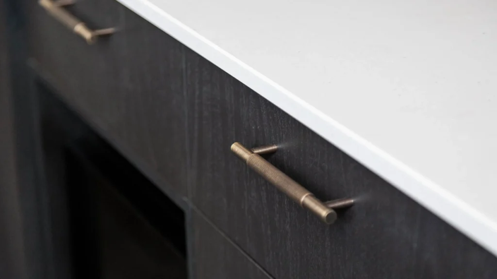 Textured bronze bar pull on a dark wood grain custom kitchen drawer under a white countertop in a luxury villa.
