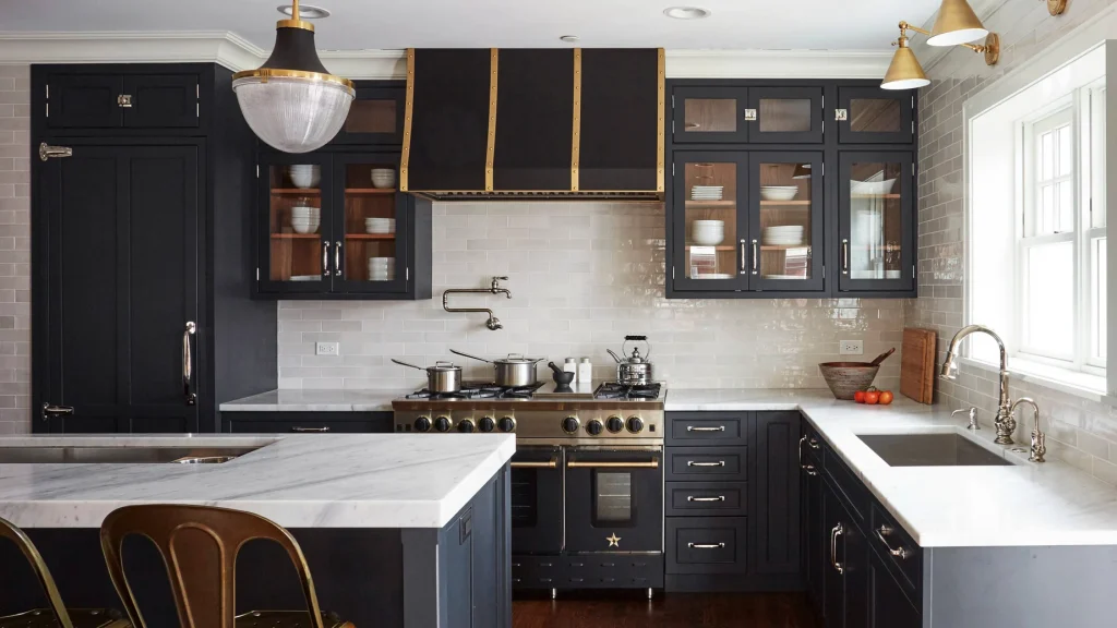Matte charcoal kitchen cabinets with light marble countertops, a white tile backsplash, and a black and brass range hood.