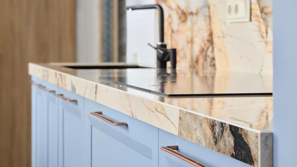 Custom light blue cabinets with copper handles, paired with a polished veined beige marble countertop and black faucet.