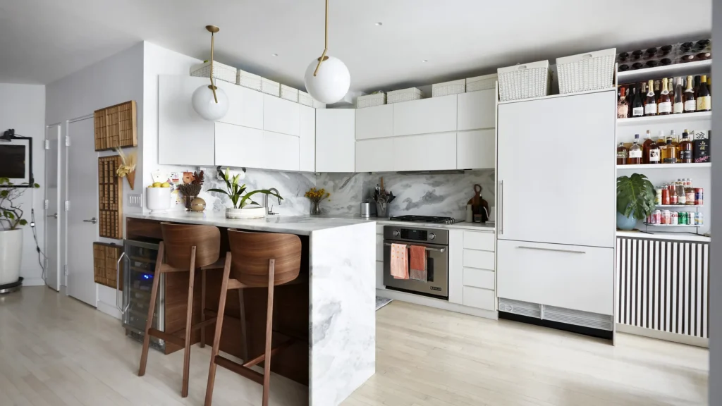 Uniform white woven storage baskets with lids above modern white kitchen cabinets and a marble waterfall island.