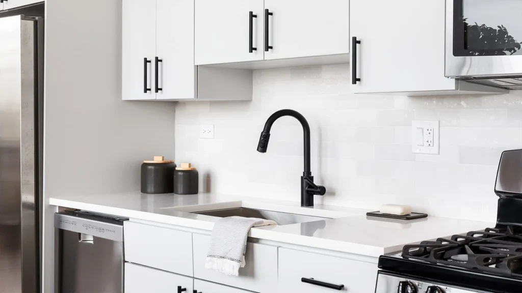 Matte black T-bar pulls and matching black faucet on modern white custom kitchen cabinets in a sleek apartment.