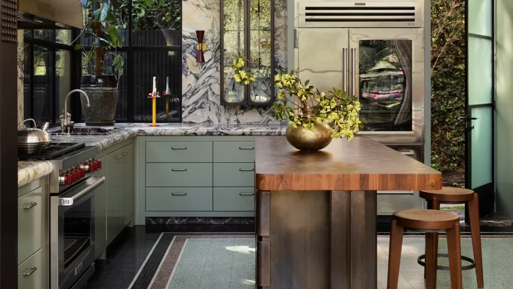 Muted sage green kitchen cabinets with a thick marble backsplash, paired with a wood-top island and bar stools.