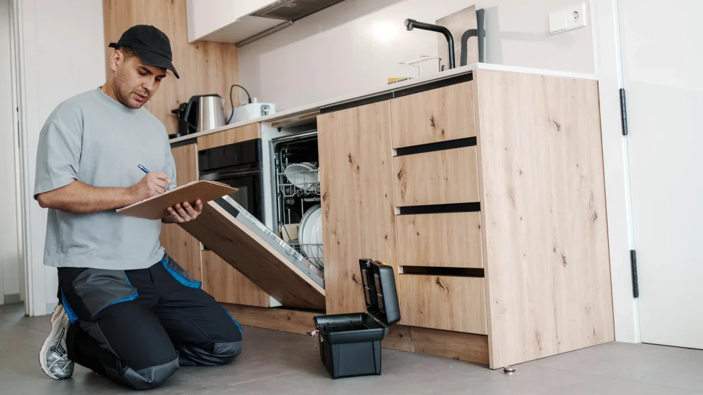 A technician conducting a quality check on custom light wood kitchen cabinets and an integrated dishwasher system.