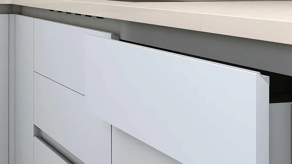 Sleek silver edge pulls mounted on minimalist white flat-panel kitchen drawers for a handleless look.