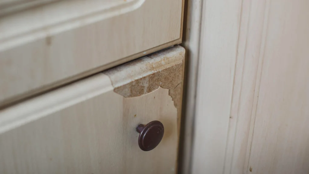Peeling laminate finish on a beige MDF cabinet drawer, showing poor adhesion on a high-wear corner.
