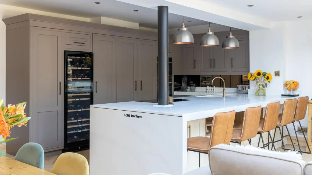 Large white quartz island with seating over 36 inches deep, matching a taupe tall cabinet wall with a built-in wine cooler.
