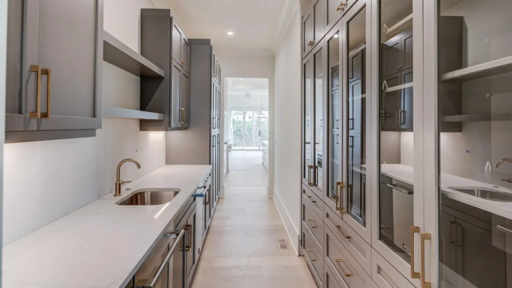 Narrow luxury butler's pantry with gray custom cabinets and glass doors, optimizing layout depth in a villa home.